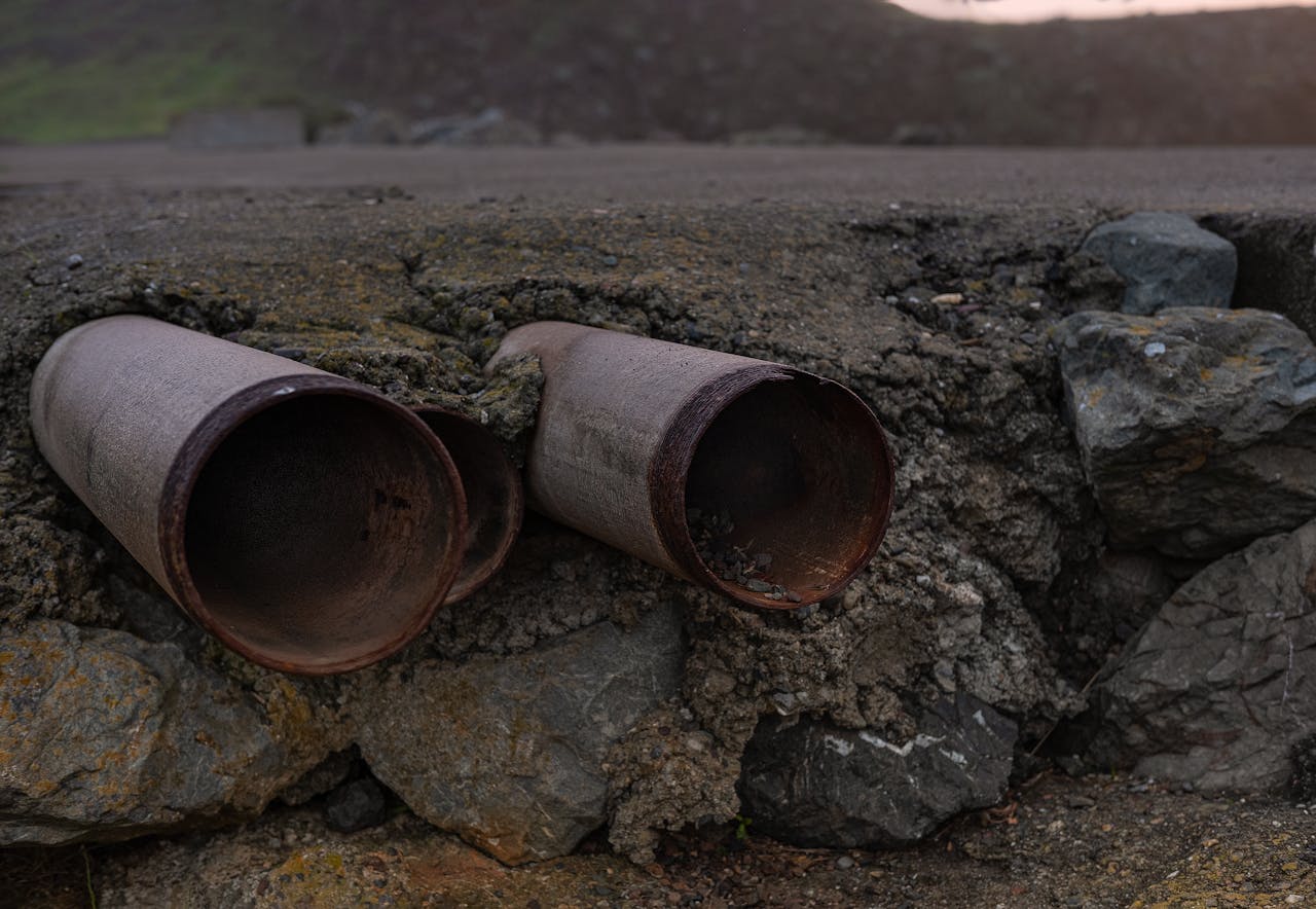 who-we-are Close-up of two rusty steel pipes protruding from a rocky surface, showcasing erosion and weathering effects.