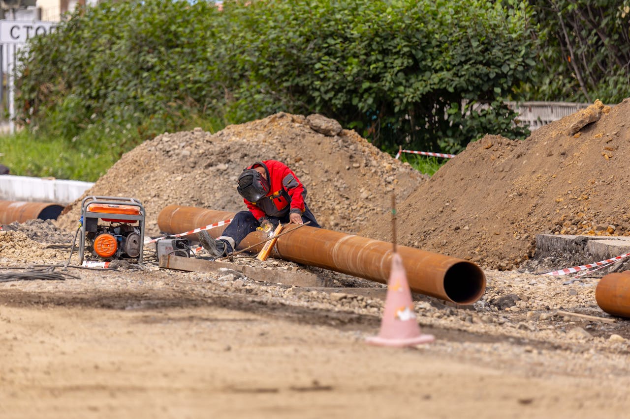 journey A construction worker welds a large pipe on a sunny day at an outdoor site.